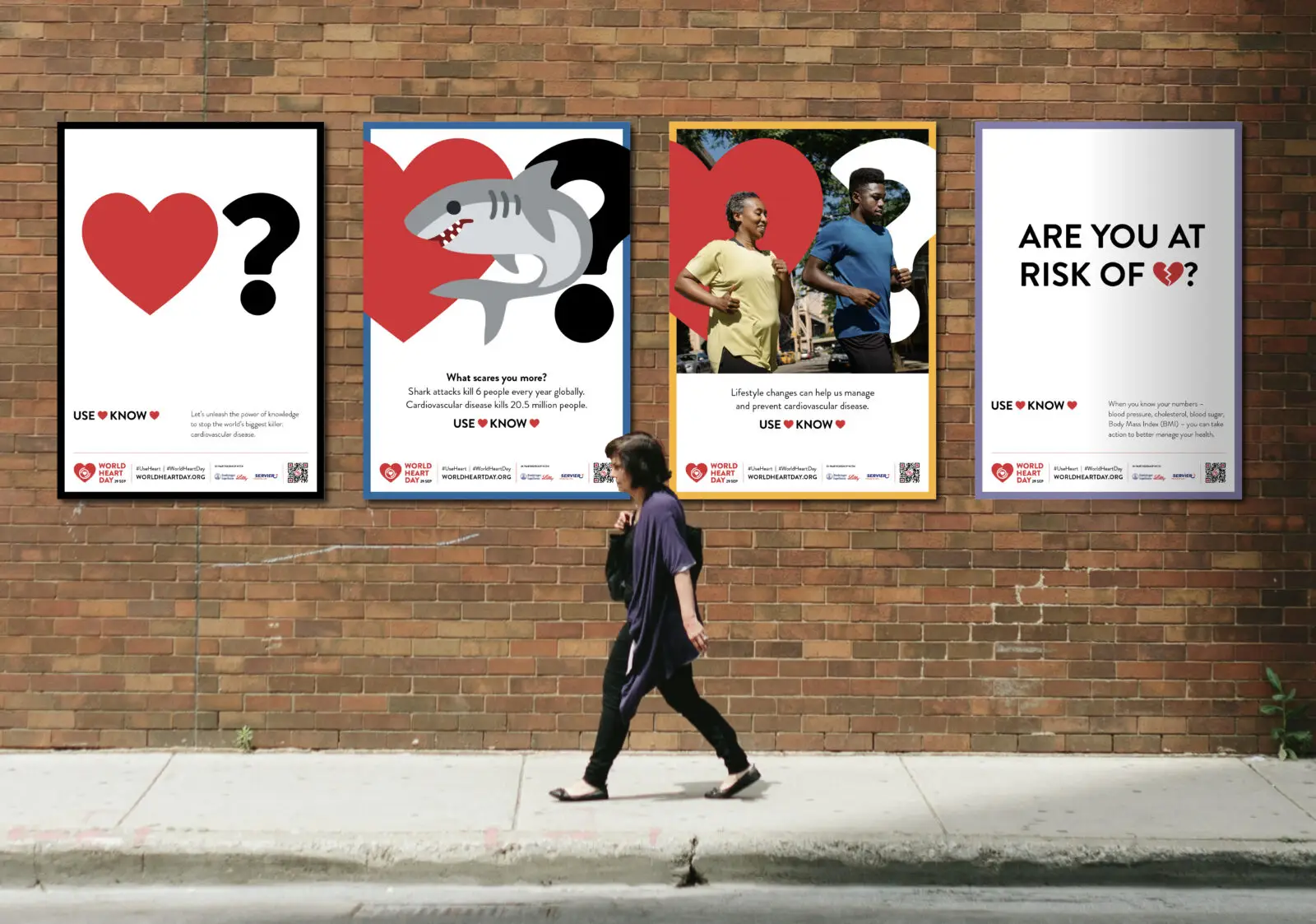 a woman walking past four world heart day campaign posters on a bricked wall