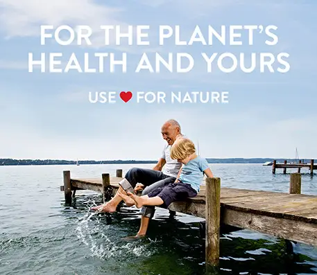 Dad and a son sat on a jetty in a large lake splashing their feet with the text For the Planet's Health and Yours Use Heart for Nature