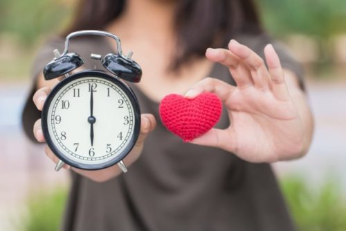 A woman holding an alarm clock and a knitted heart