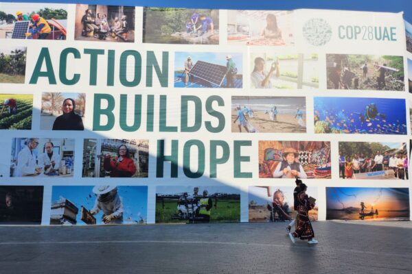Action Builds Hope COP28UAE Banner with 2 people walking in front of it - WHF Welcomes COP28 Agreements