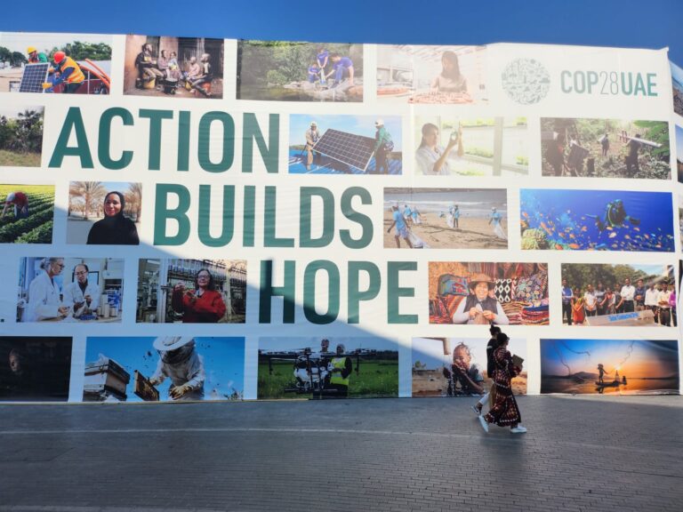 Action Builds Hope COP28UAE Banner with 2 people walking in front of it - WHF Welcomes COP28 Agreements