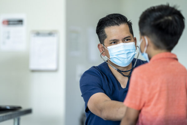 a male medical professional wearing a face mask is using a stethoscope to examine a young boy