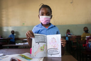 A young child in school wearing a covid mask with colouring in a colours to save hearts book