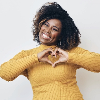 Woman in a yellow jumper and making a heart shape with her hands on her chest