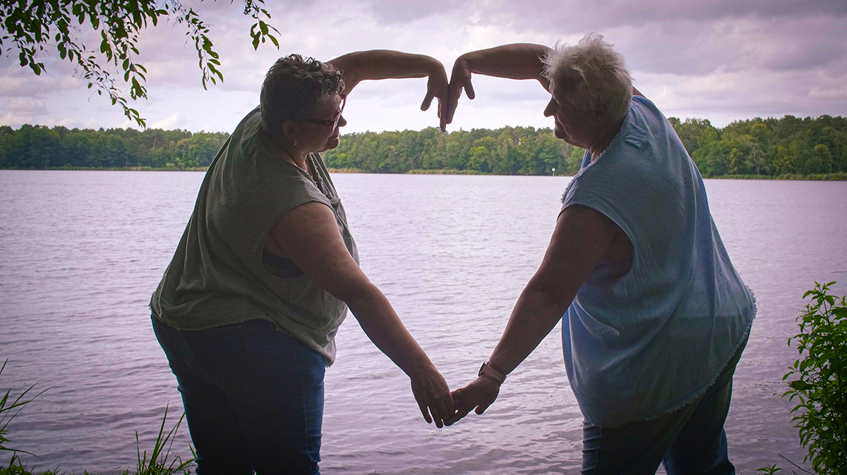 2 women making a heart shape with their arms in front of a lake beats of change film series