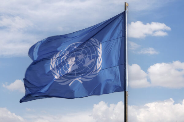 A blue United Nations flag blowing in the wind with a blue sky and clouds in the background
