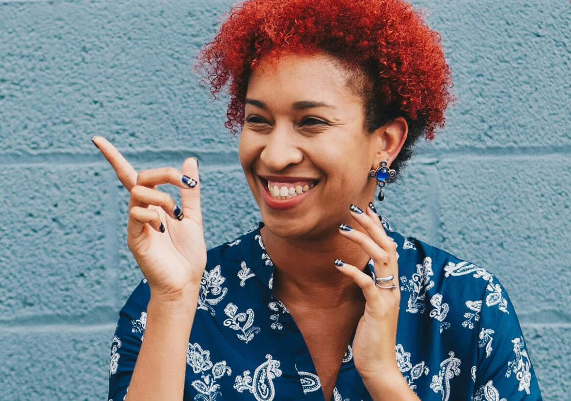 A lady with red hair smiling and pointing with a cut out heart shaped red banner for world heart day