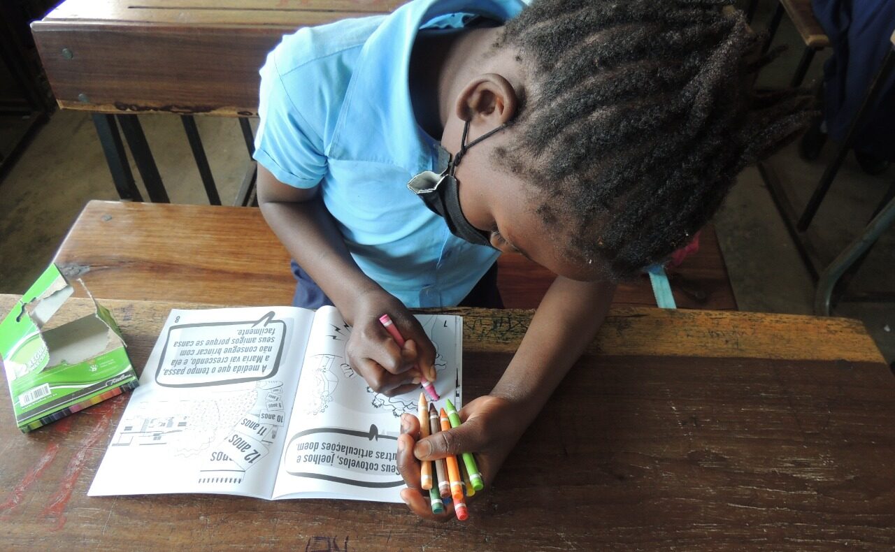 Una niña que llevaba una mascarilla estaba sentada en un pupitre del colegio coloreando un libro con lápices de colores.