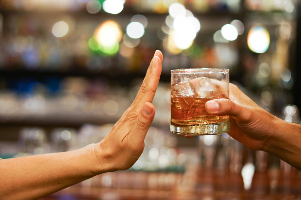 photo showing a short drink of liquor being passed in a glass with ice being refused by the intended recipient