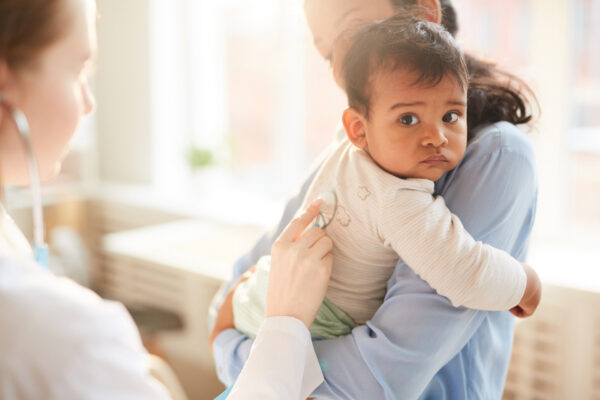 A mother is holding her toddler while a medical professional is using a stethoscope to examine - Familial Hypercholesterolemia