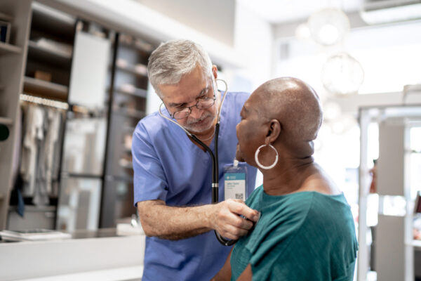 Senior male doctor using stethoscope to examine elderly woman during medical consultation