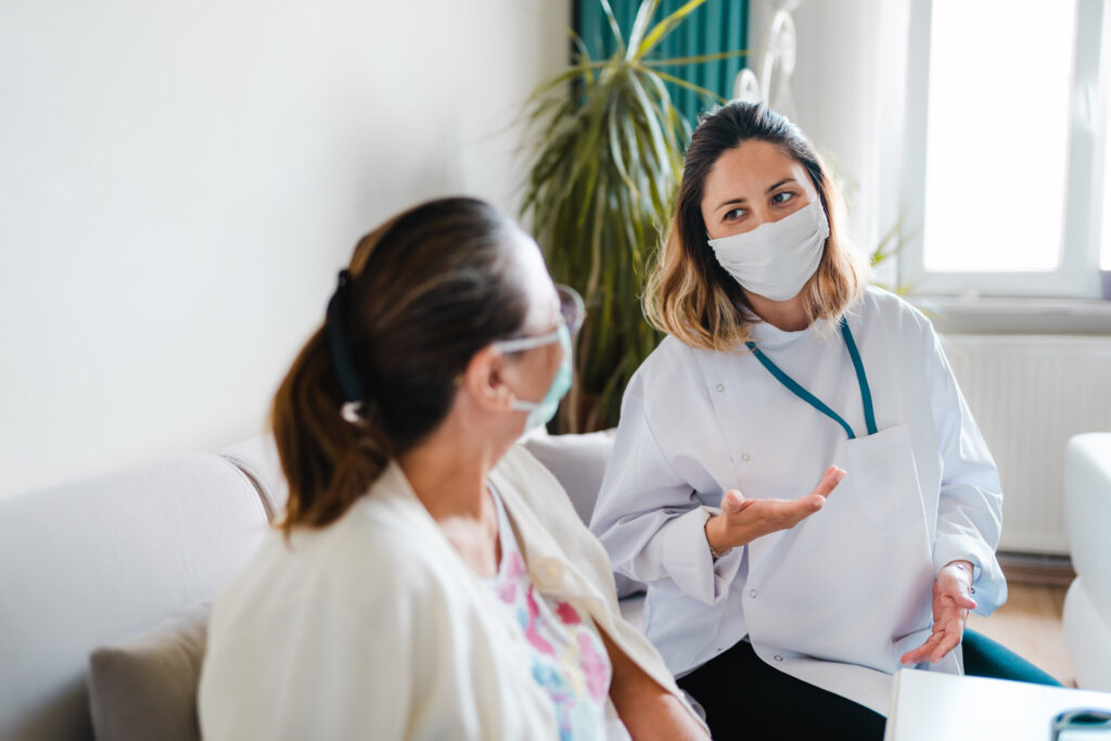 Female doctor wearing a face mask talking to a patient during a home healthcare visit