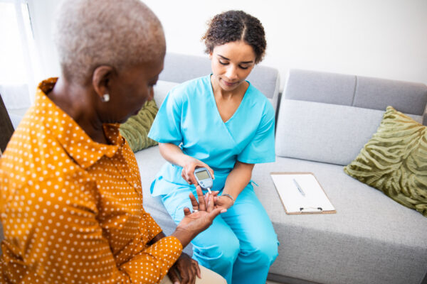 Healthcare worker checking blood sugar levels of an elderly woman using a glucometer at home