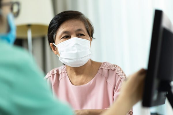 A medical doctor is showing results to a female patient wearing COVID-19 face masks on screen.