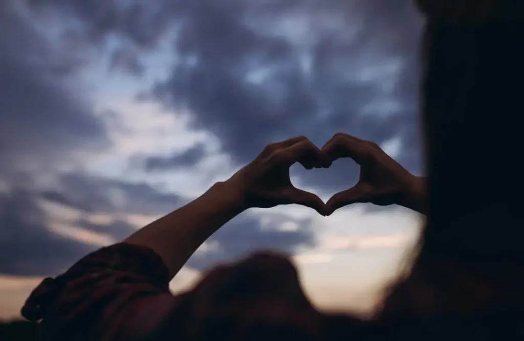 Female hands making the shape of a heart over a sunset sky