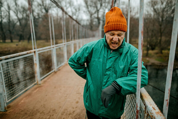 an elderly gentleman leaning on a bridge to take a breath after a walk on an cold, overcast day