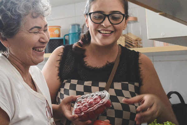 Healthy eating for heart health - 2 ladies in a kitchen laughing whilst cooking, holding fruit and vegetables