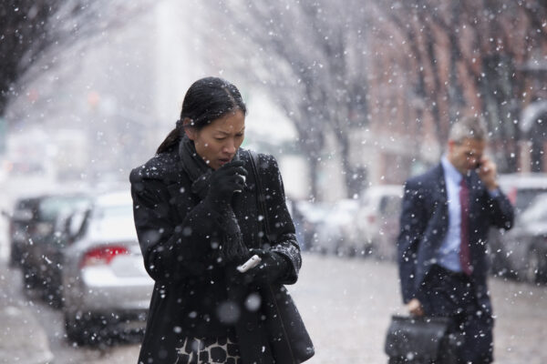 a woman walking along a street in the street, wrapped up while coughing
