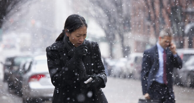 a woman walking along a street in the street, wrapped up while coughing