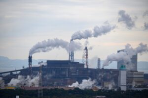 An image depicting air pollution. The image shows 3 chimneys showing lots of smoke, and a factory beneath