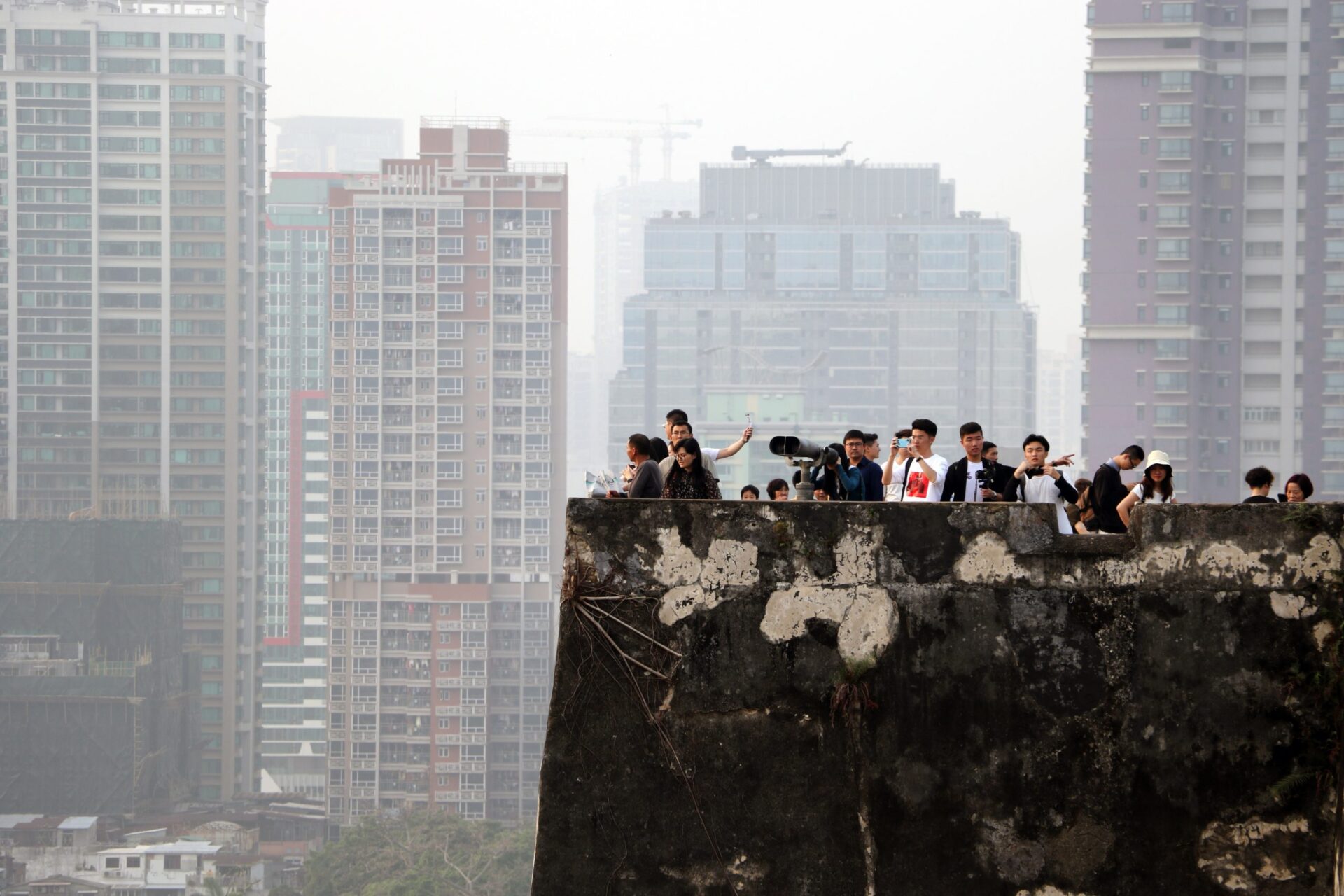 An image of a group of people looking off the roof of a multi-storey building. In the distance are more multi-storey buildings