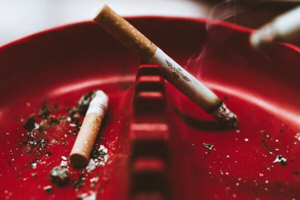 A photo of two cigarettes sat in a red ash tray