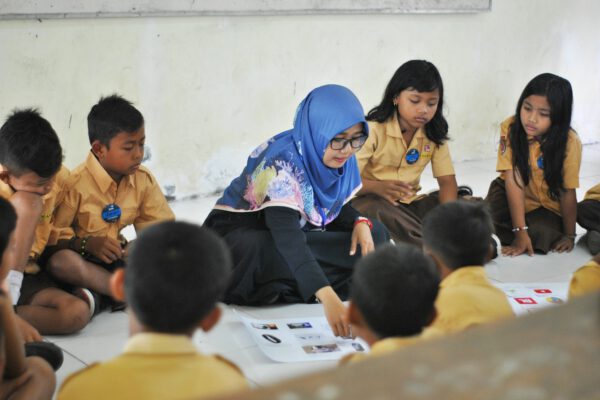 A teacher educating young students while sat on the floor