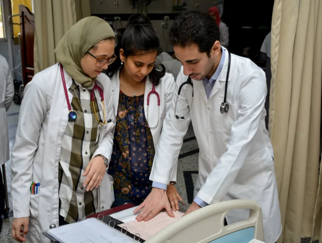 Three medical professionals reviewing patient charts together in a hospital setting, wearing white lab coats and stethoscopes