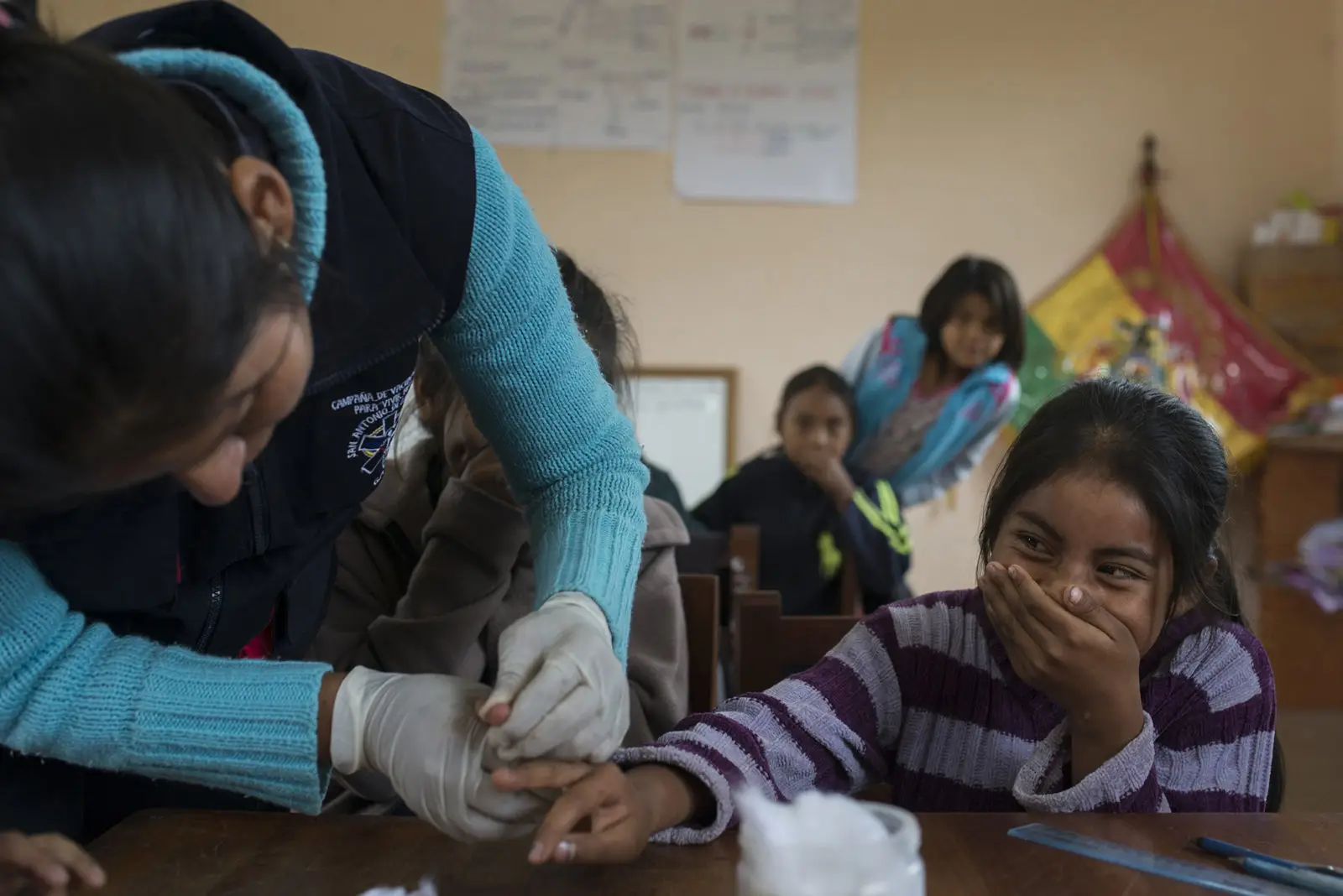 Healthcare professional checking a little girls fingers whilst the girl is covering her mouth laughing - screening for Chagas