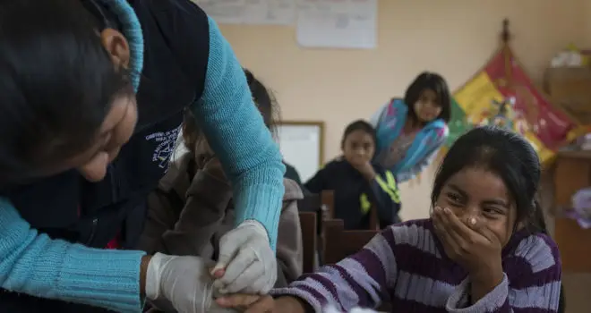 Healthcare professional checking a little girls fingers whilst the girl is covering her mouth laughing - screening for Chagas