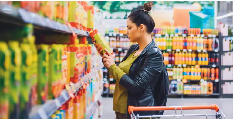 A picture of a woman in a supermarket looking at the information on the back of a juice carton