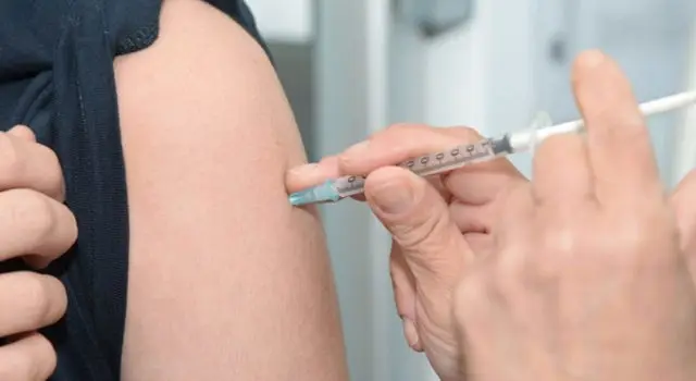A close-up of a healthcare professional administering a vaccine injection into a person's upper arm using a syringe.