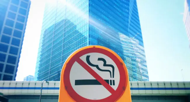 A no smoking sign placed infront of a skyscraper
