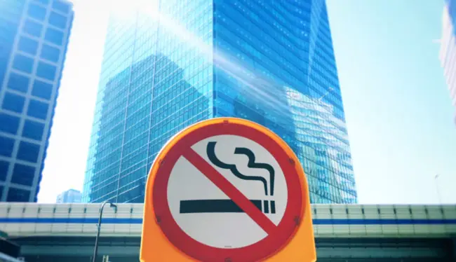 A no smoking sign placed infront of a skyscraper