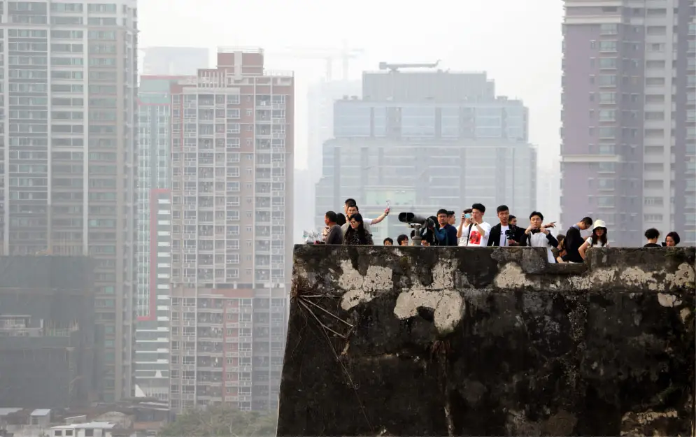 An image of a group of people looking off the roof of a multi-storey building. In the distance are more multi-storey buildings
