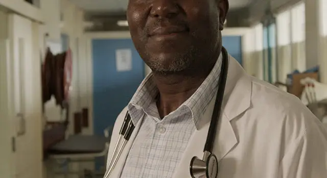 Confident male doctor wearing white coat and stethoscope standing in hospital corridor