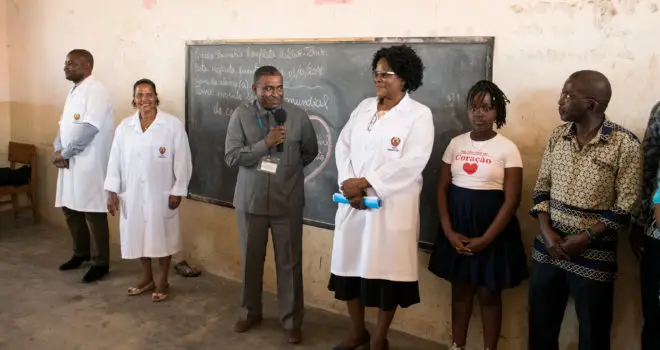 Health care professionals and other people at the front of a classroom, man holding a microphone in front of blackboard.