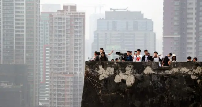 An image of a group of people looking off the roof of a multi-storey building. In the distance are more multi-storey buildings