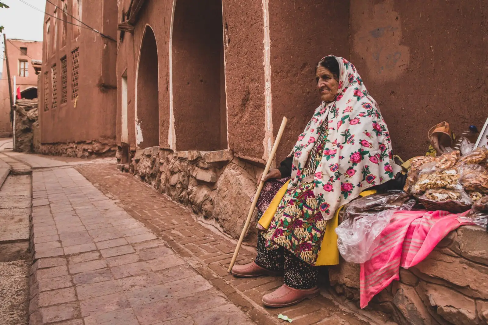 Elderly woman from the eastern mediterranean region sat on a wall holding a stick