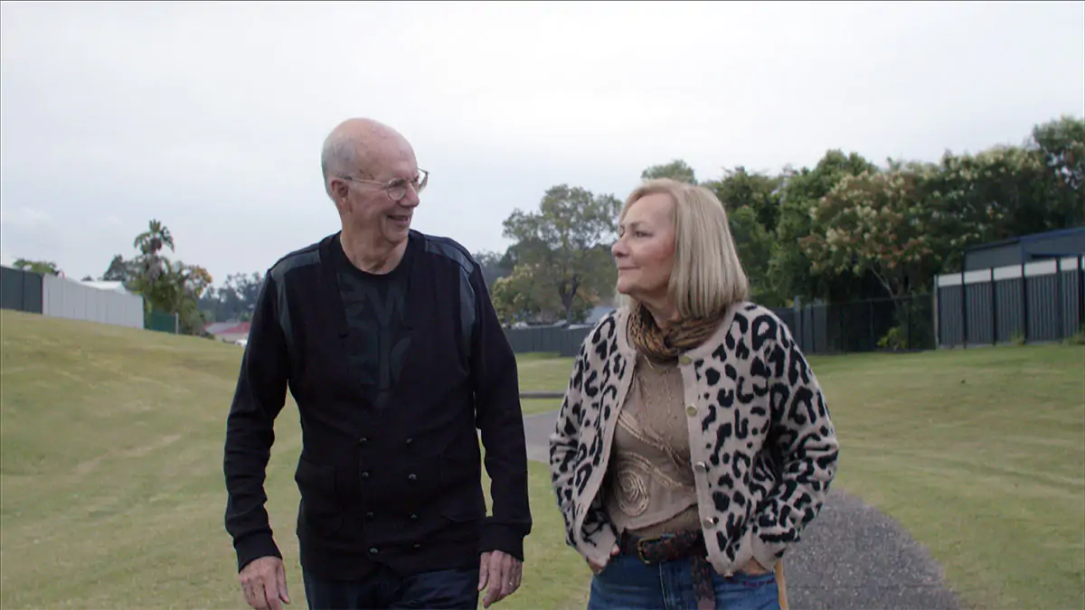 Beats Of Change - An older couple walking across a grass field smiling at one another