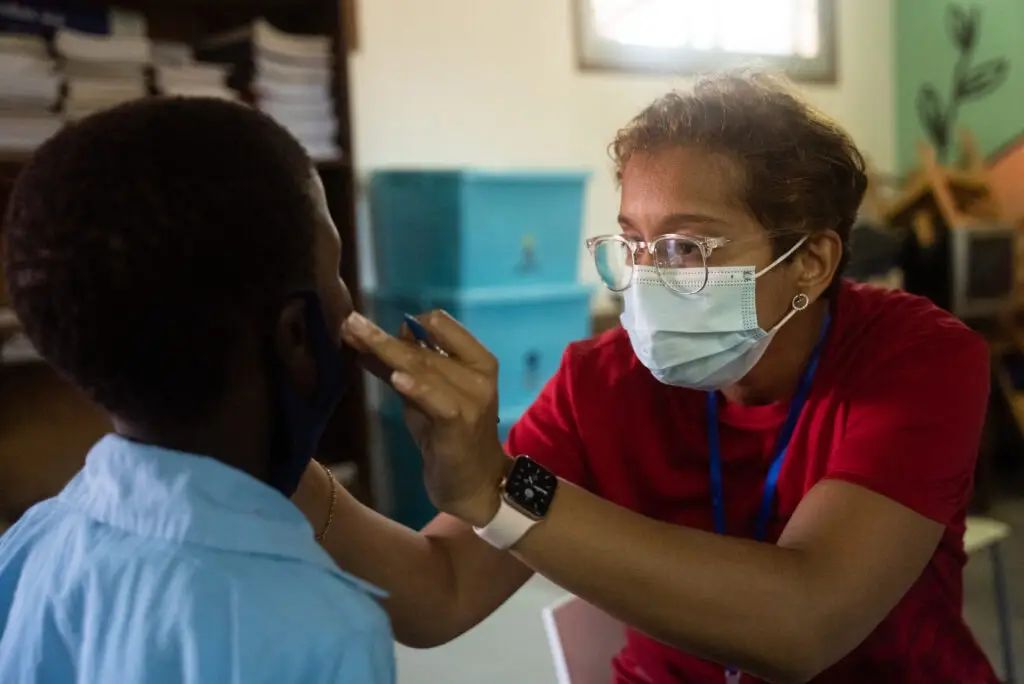 A health professional, wearing a covid mask is examining a young male