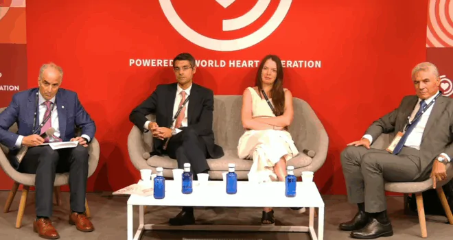 Four panelists seated on stage in front of a red backdrop reading ‘Powered by World Heart Federation,’ engaged in discussion with water bottles and microphones on a table in front.