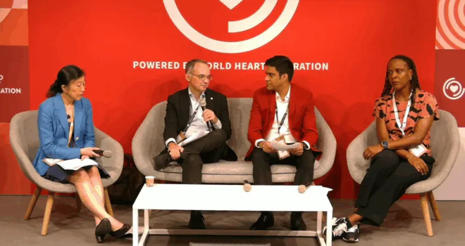 Four panelists seated on stage in front of a red backdrop reading ‘Powered by World Heart Federation’; two men in the centre, one woman on each side, all holding microphones or notes, engaged in a discussion.