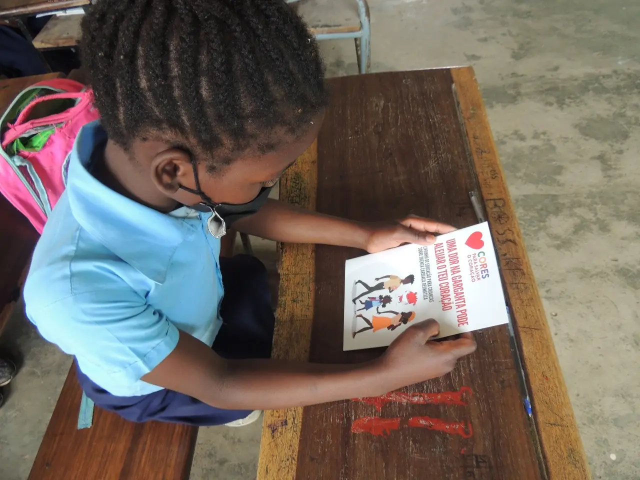 a young child wearing a facebook is reading a Colours to Save heart booklet in Maputo, Mozambique