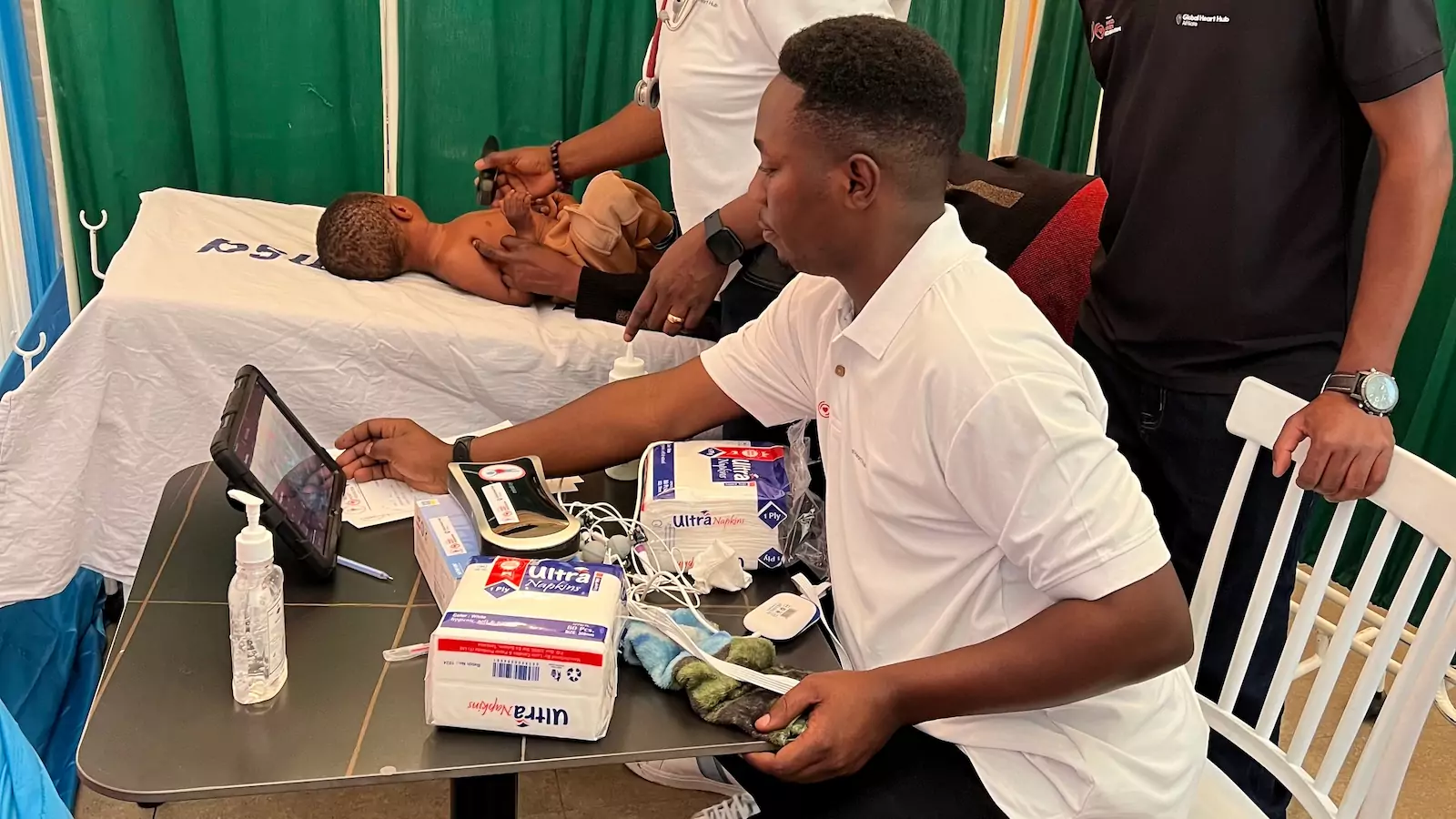 Little boy is being under going medial tests whilst laid on a medical bed. The professional is reviewing the data on a tablet device.