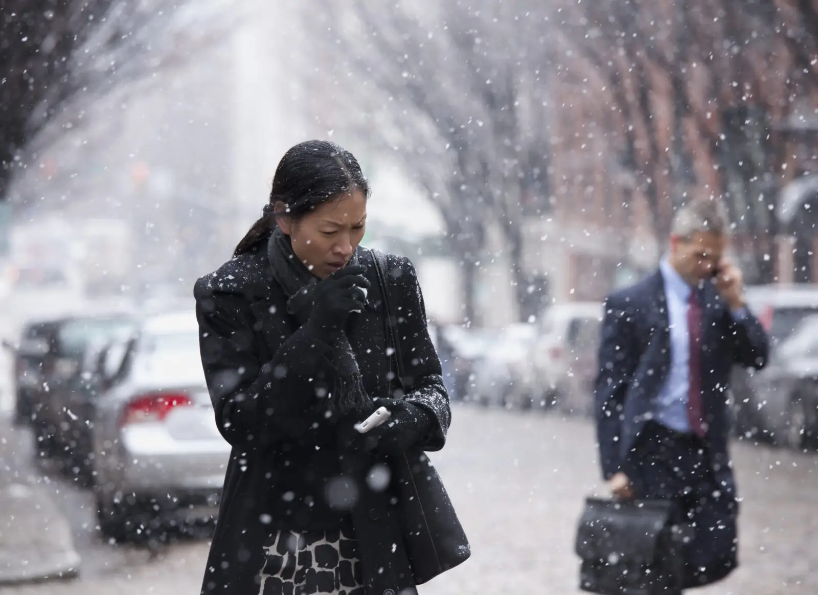 a woman walking along a street in the street, wrapped up while coughing