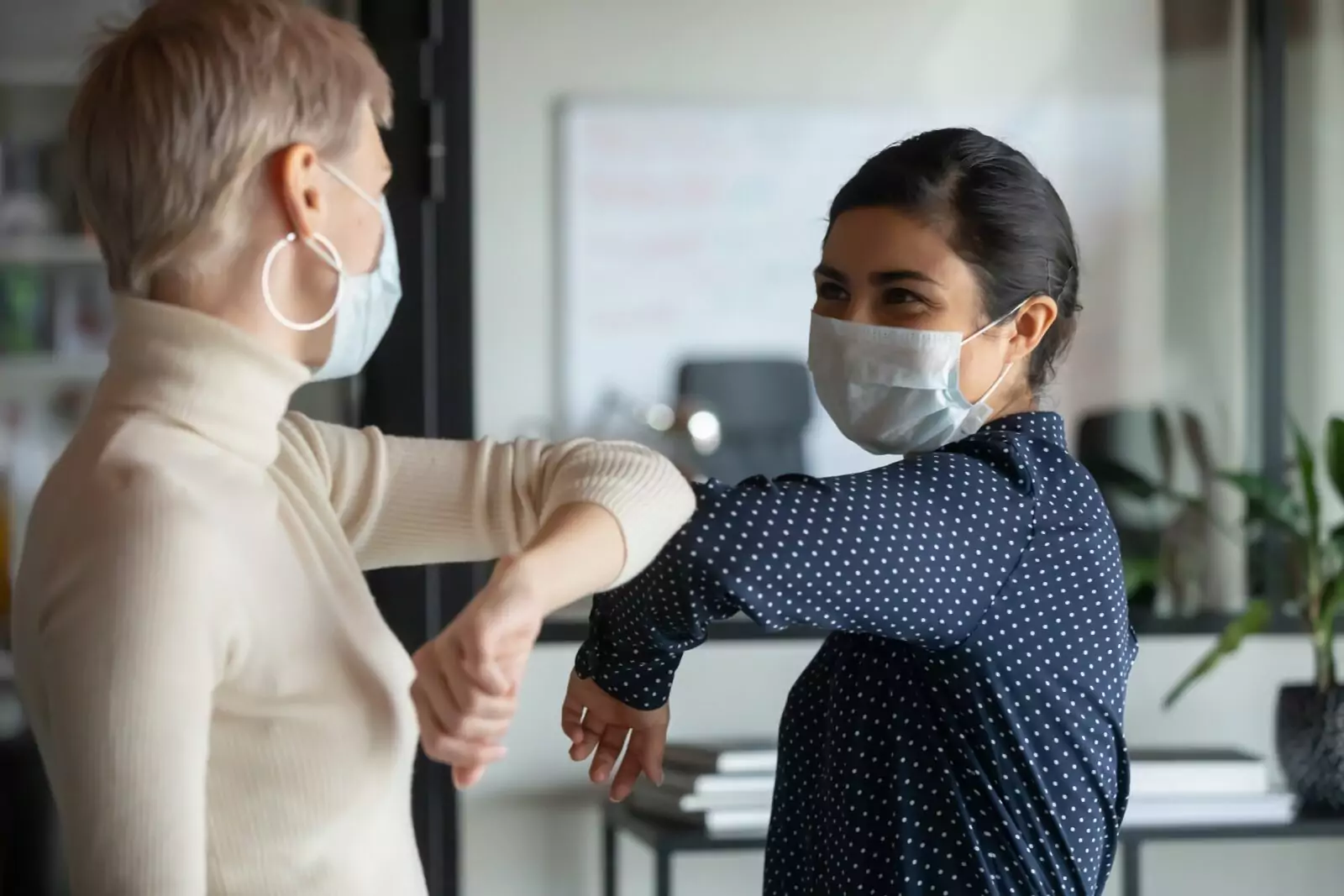 Two ladies touch elbows to greet each other in passing.